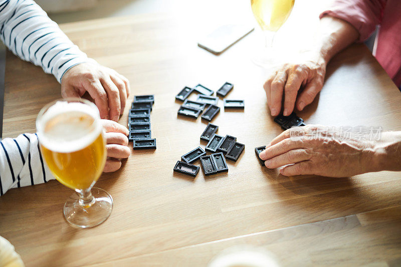 不认识的老男人坐在木桌和玩多米诺骨牌，而喝啤酒在酒吧，他们选择多米诺骨牌而开始游戏
