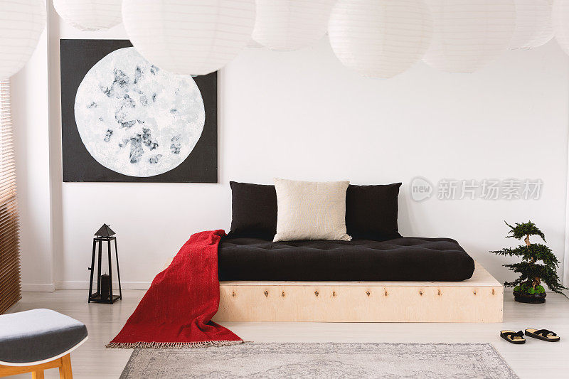 卧室内的木床上有黑色的床单和红色的毯子，还有月亮海报。真实的照片