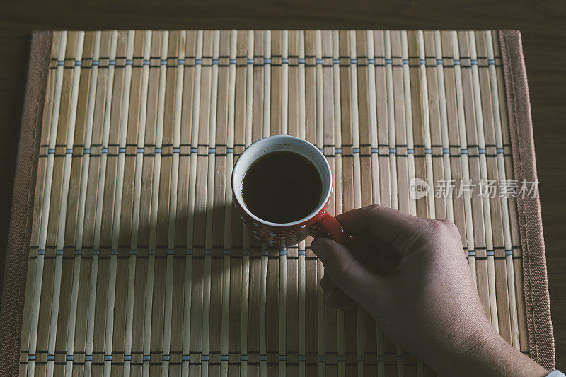 人的手拿着桌子上的黑咖啡杯。高角度视角，个人视角。