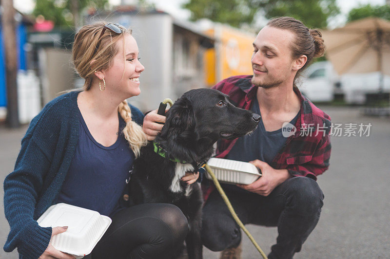 一对年轻夫妇抱着他们的狗和食品车上的打包盒摆姿势
