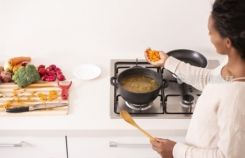 女人做饭时，将切碎的胡萝卜放入沸腾的汤锅中。