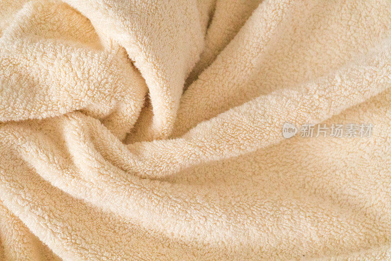 蓬松的米色毛巾背景，特写。柔和的婴儿色的织物，波浪和褶皱。褶皱柔嫩，毛巾质地淡橙色。沐浴蓬松的毛巾，水疗背景