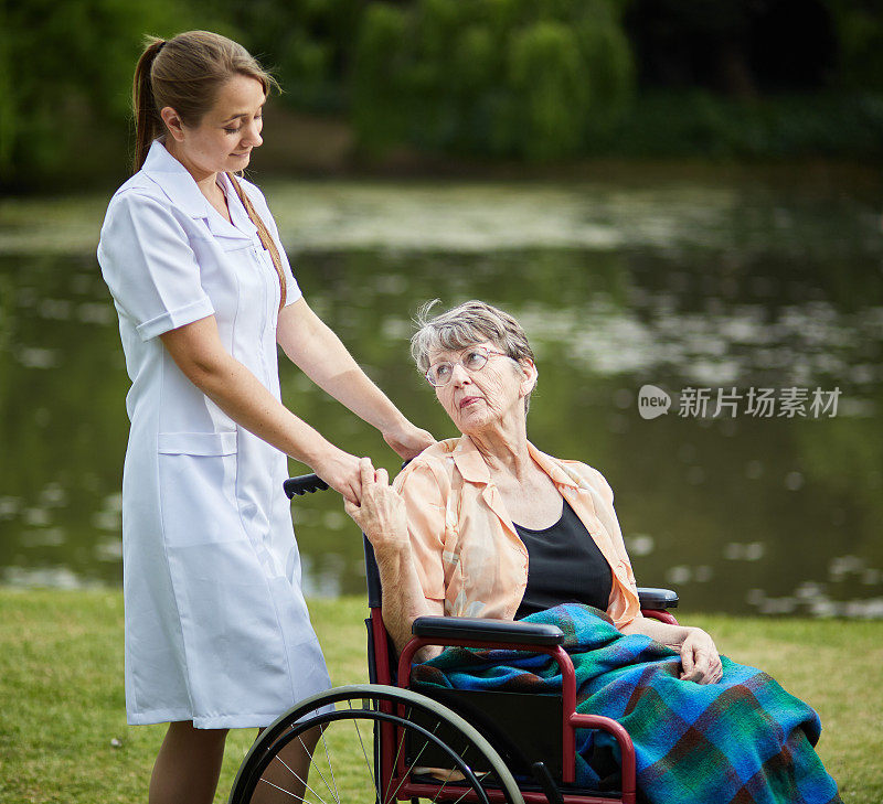 坐在轮椅上的老年妇女和她的护理助理一起去公园郊游