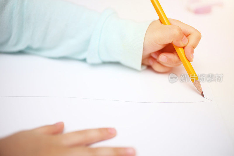 一个孩子的手与铅笔在纸上画的特写