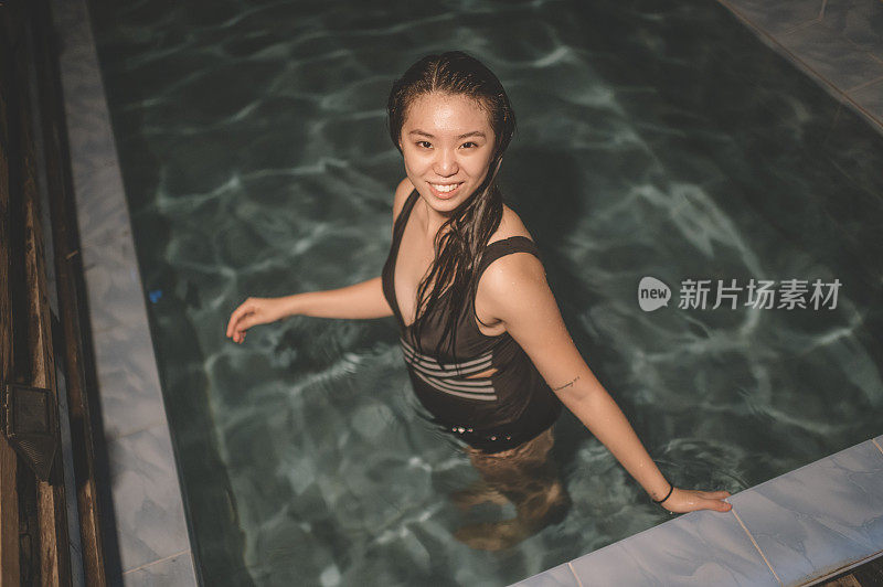 一个亚洲华裔少女晚上在自家门前的游泳池里游泳