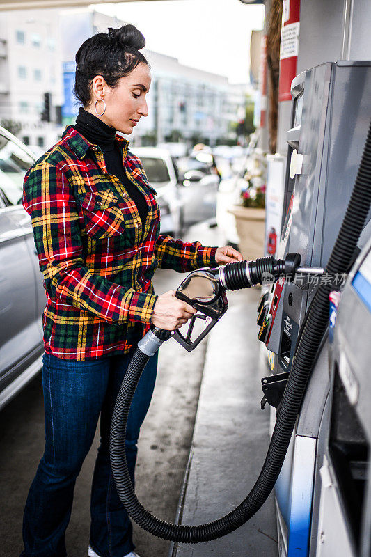 一个现代妇女在加油站拿着一根燃料软管