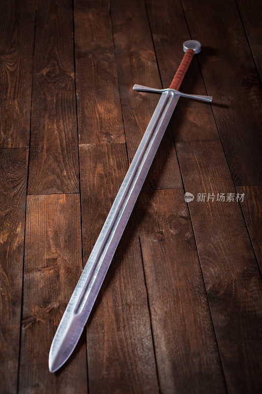 木桌上放着一把金属剑，柄为棕色，配有特殊的护具。