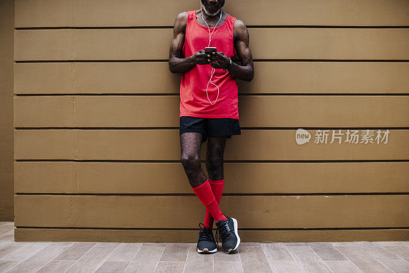 年长非洲裔美国人在红色运动服听音乐在他的手机休息从他的晨跑
