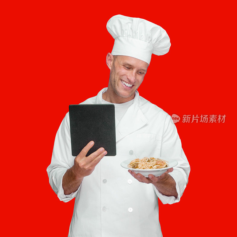 白人年轻男厨师在有色背景下穿着裤子，使用触摸屏