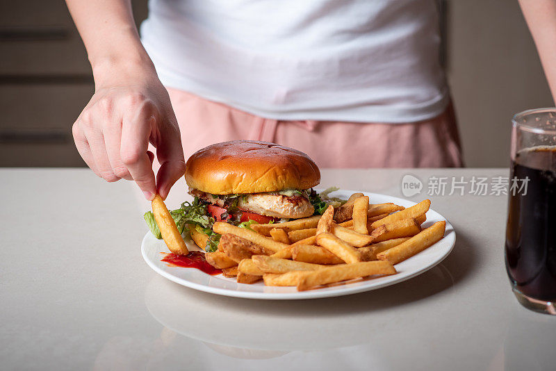 一个女人吃着盛在盘子里的鸡肉汉堡和炸薯条