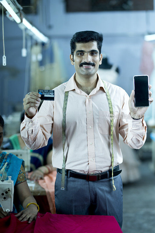男裁缝在纺织厂展示手机和信用卡