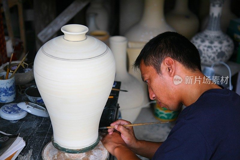 中国江西景德镇，一名工人在古陶瓷窑上为一个瓷罐作画和装饰