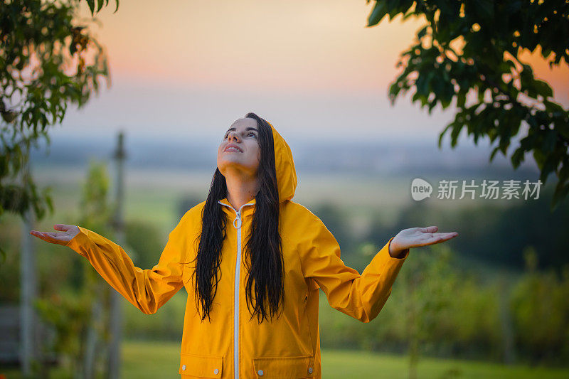 穿雨衣的女人伸开双臂抬头看。年轻女子在享受雨。