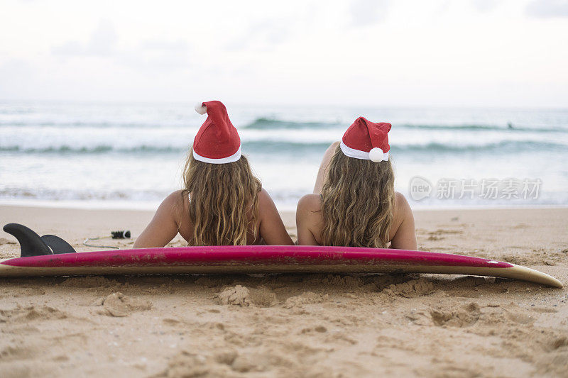 圣诞节，两个戴着圣诞老人帽子的年轻女子在海滩上晒太阳