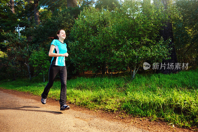 年轻的女性跑步者在一个美丽的阳光灿烂的森林里锻炼