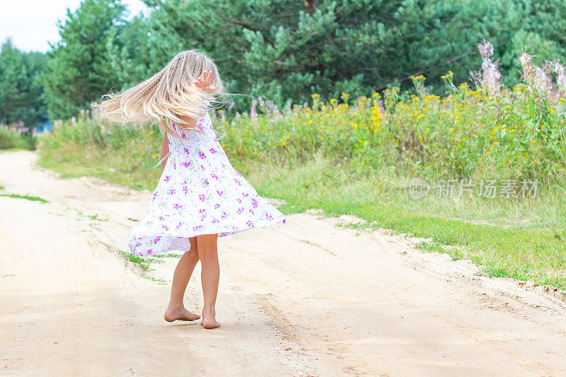 一个长着金色卷发的女孩在森林的路上跳舞。童年，快乐，自由运动，舞蹈，与自然团聚。