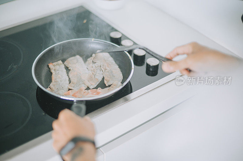 亚洲华人高级男子在厨房的炉灶上烹饪培根在准备早餐