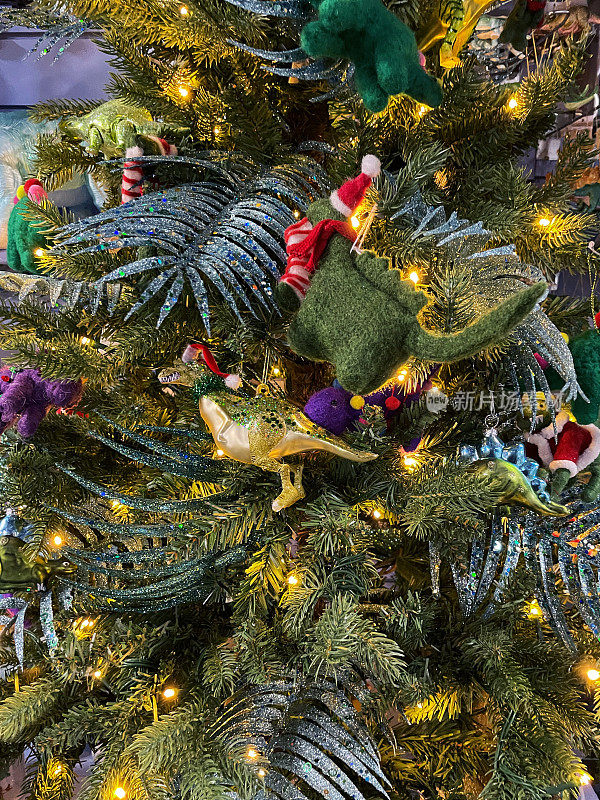特写个体，雷克斯暴龙装饰品挂在人造圣诞树的树枝上，闪闪发光的树叶，云杉针，模糊的白色精灵灯