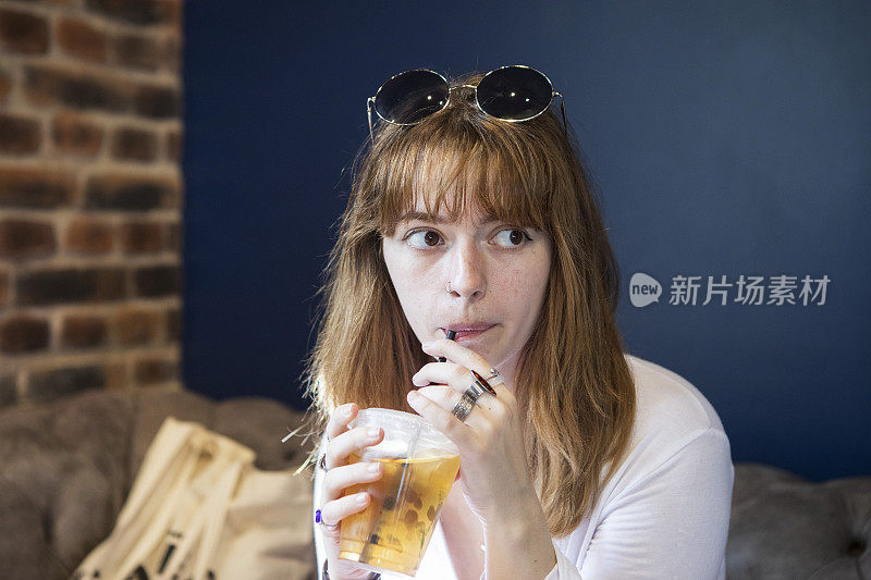 一个年轻的女人在咖啡馆里喝着冰茶，看着旁边的人