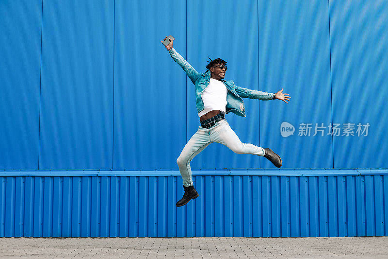 一个非洲人拿着电话跳了起来，在城市的蓝色建筑的背景下