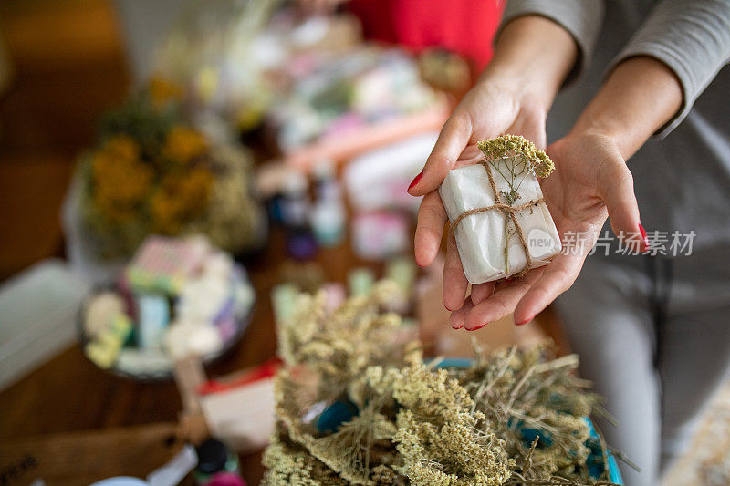 一个年轻的女人在她的家庭作坊里拿着包装好的天然油手工制作的肥皂