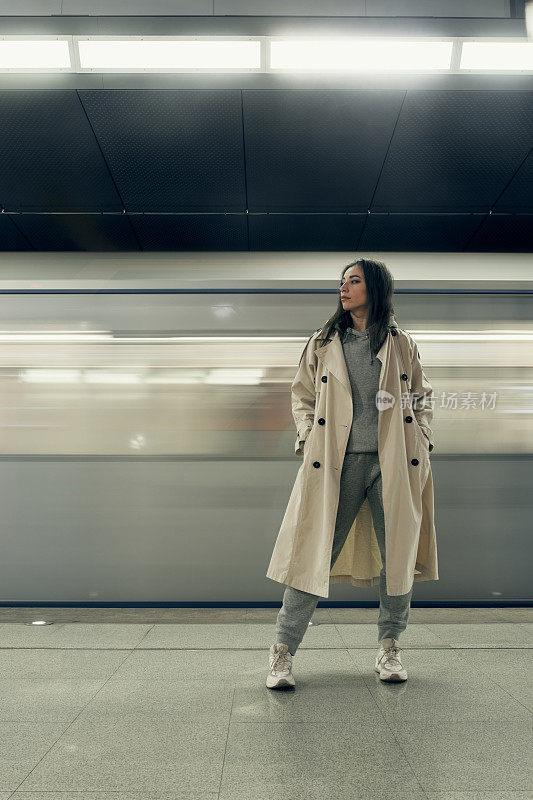 穿着米色风衣的女孩在地铁站台上等车