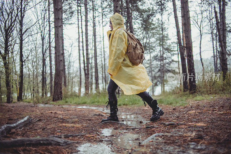 一个快乐的年轻女子在一个下雨天穿着一件黄色雨衣在树林里享受大自然。