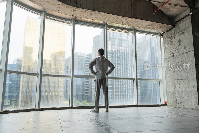 一个亚洲人站在一间新办公室的大落地窗旁