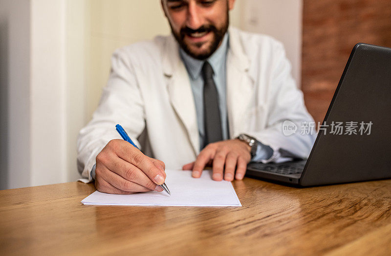 一位留着胡子的年轻医生正在为他的病人填写表格。他坐着在面前的模版上写东西。