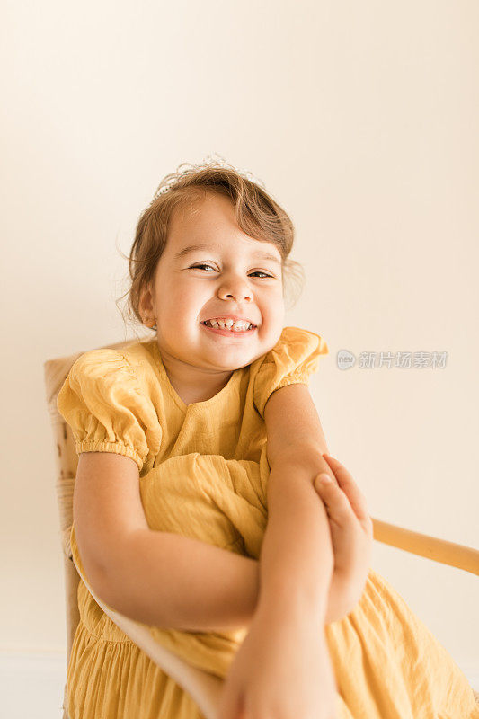 一个将近3岁的幼童，棕色卷发和棕色眼睛，穿着黄色的连衣裙和头饰