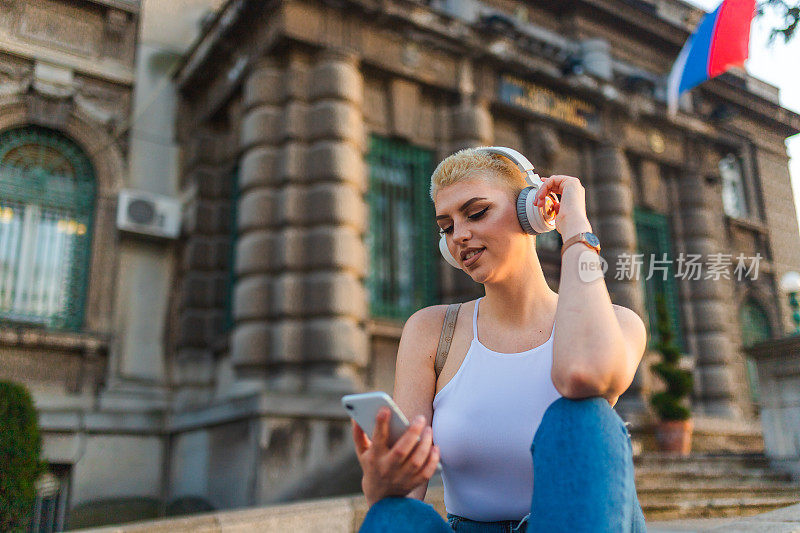 漂亮的年轻女子，短发，在城市里听音乐，用她的智能手机