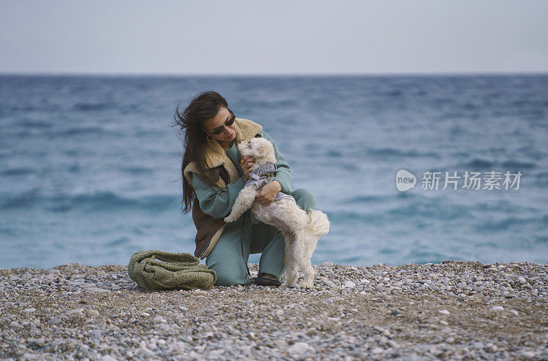 年轻女子坐在沙滩上和她的小猎犬玩耍