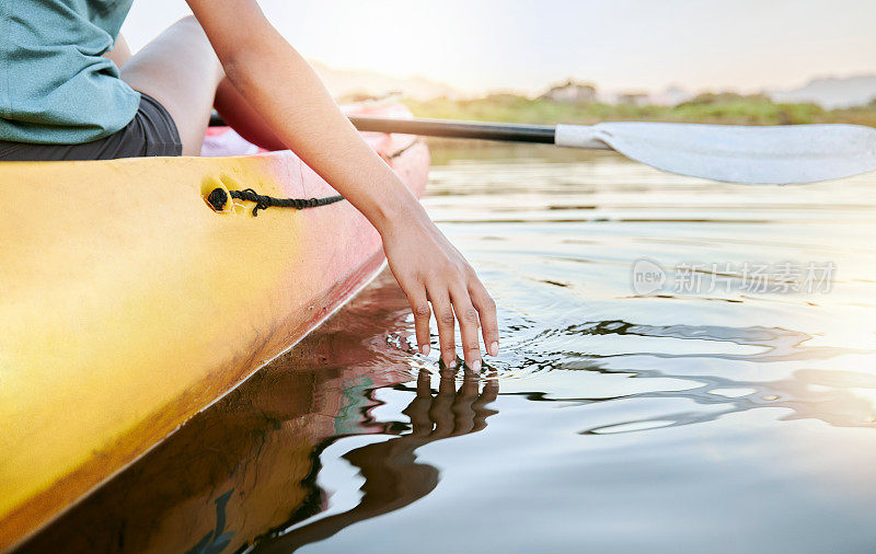 白天女性手划皮划艇和感受湖水的特写。活跃的年轻女子在夏天度假时享受水上活动。周末度假时，在平静的日落湖畔泛舟