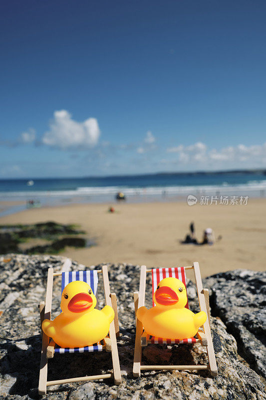 在康沃尔的纽基度假，两只橡皮鸭坐在躺椅上。在六月阳光明媚的一天，坐在一堵墙上俯瞰托湾海滩。