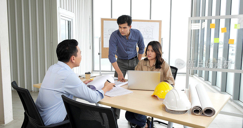 亚洲组的建筑师们在办公室的商业会议室的桌子上用蓝图制定计划，建筑师们讨论商业计划