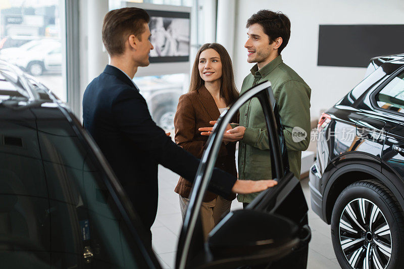 快乐的年轻夫妇咨询汽车销售员，在汽车经销商挑选新车