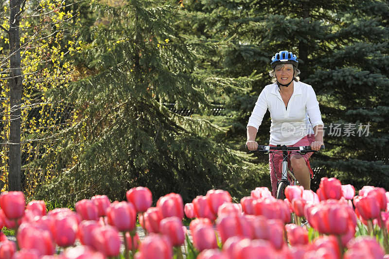 微笑的女人骑自行车靠近粉红色的花园