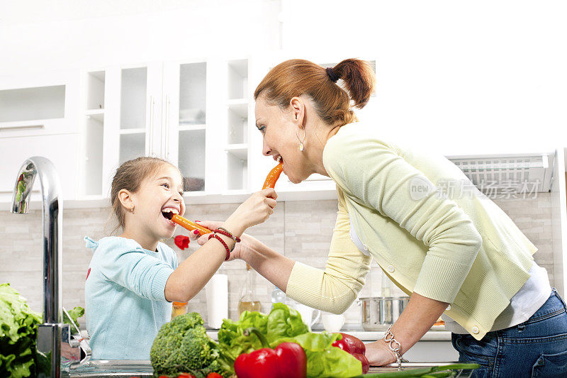 一个年轻女人和一个小女孩在厨房里吃胡萝卜