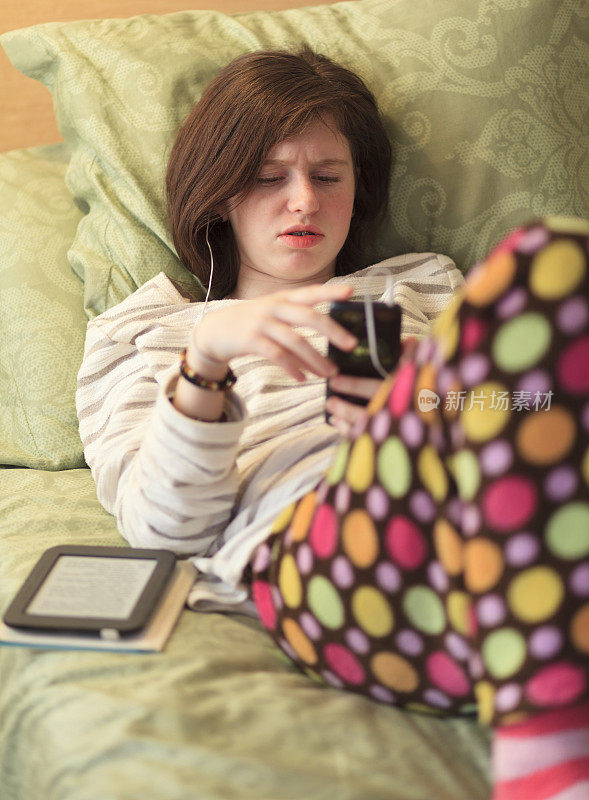 穿着睡衣的少女在床上玩智能手机