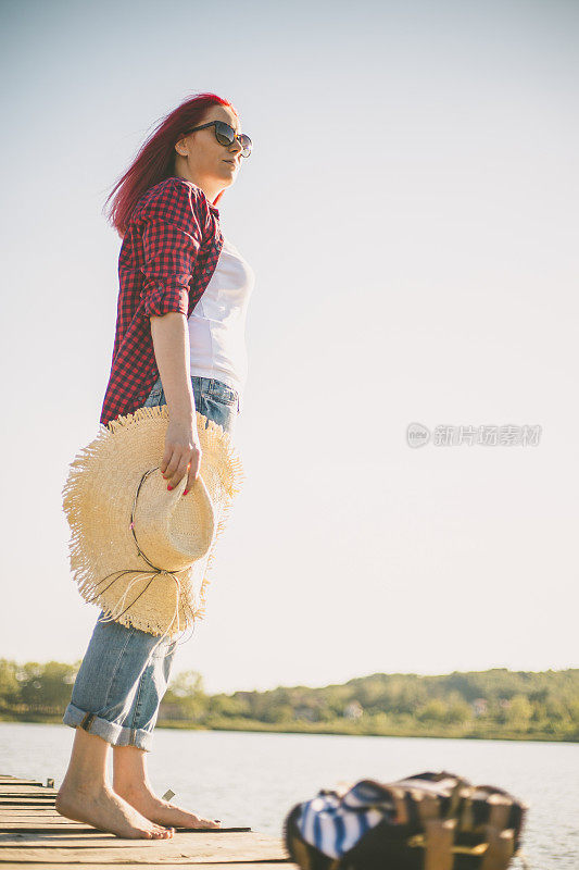 美丽的女人站在户外湖边的木码头上