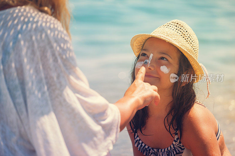 年轻的母亲在女儿脸上涂防晒霜