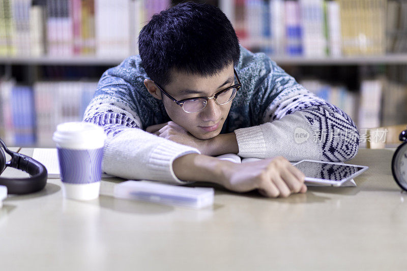 年轻的亚洲男子学生在图书馆使用平板电脑