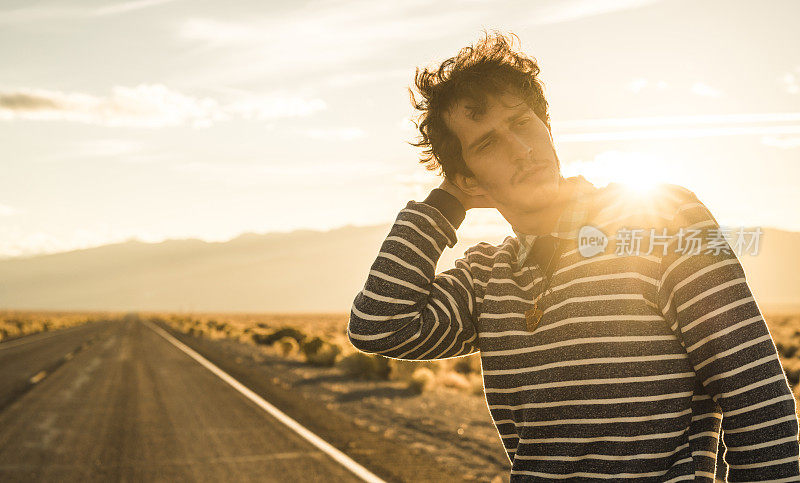 公路旅行。一个年轻人，旅行潮人，在日落时分的内华达州沙漠公路上四处张望