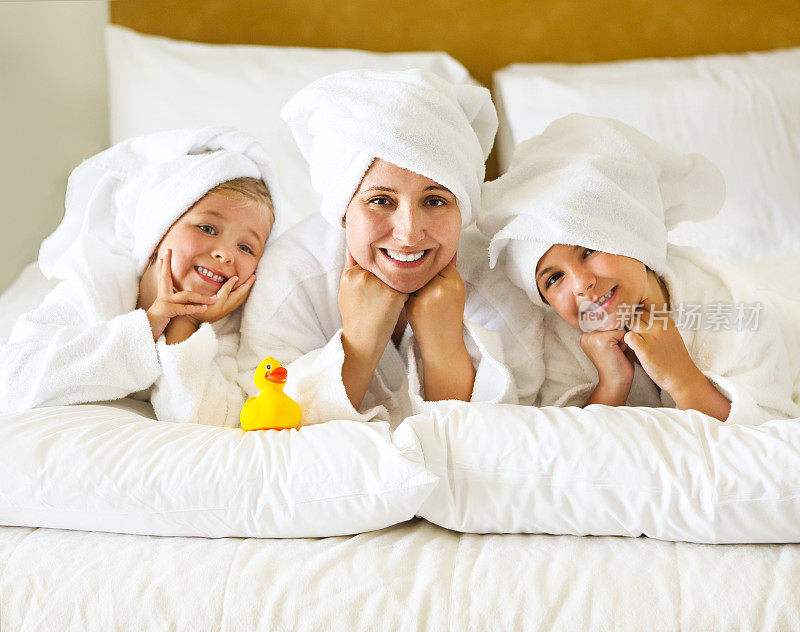 快乐的妈妈和穿着浴袍的女孩们躺在床上