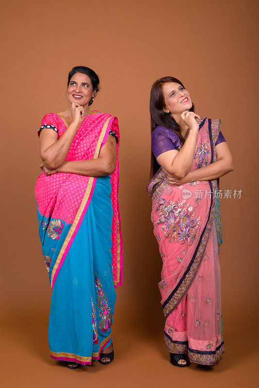 摄影工作室拍摄了两名成年印度妇女在彩色背景下一起穿着印度传统服装莎丽