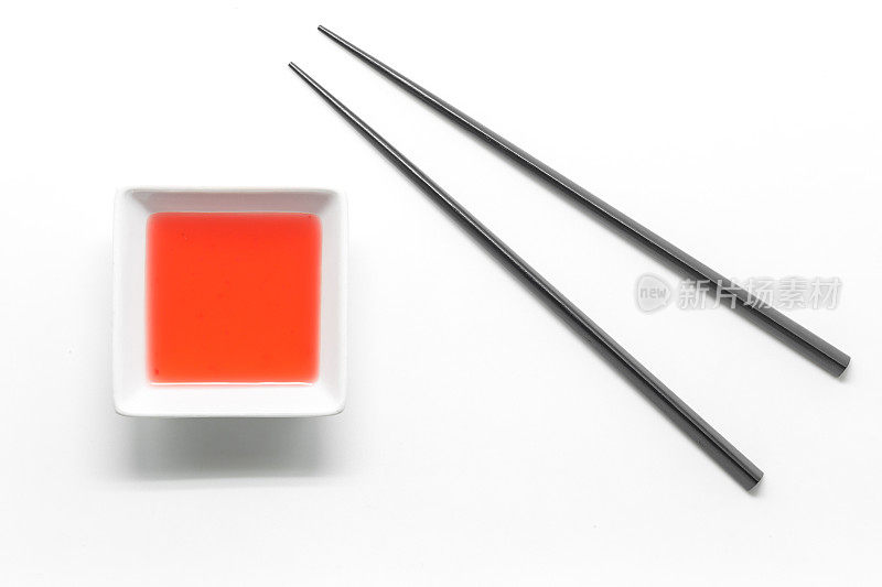 黑色木筷子和糖醋汁碗孤立在白色的背景上。