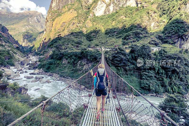 一名女子背包客穿过尼泊尔喜马拉雅山的吊桥