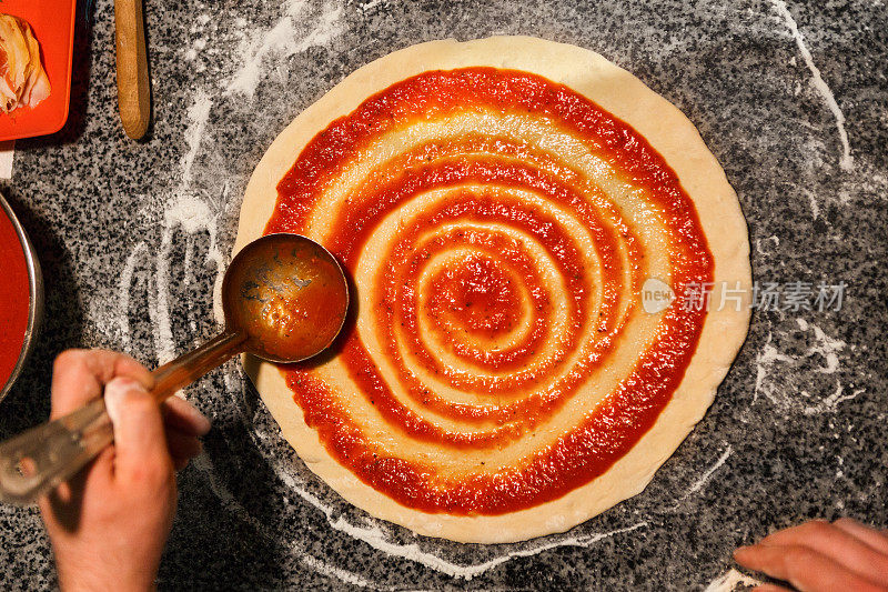 厨师亲手将番茄酱抹在披萨底上