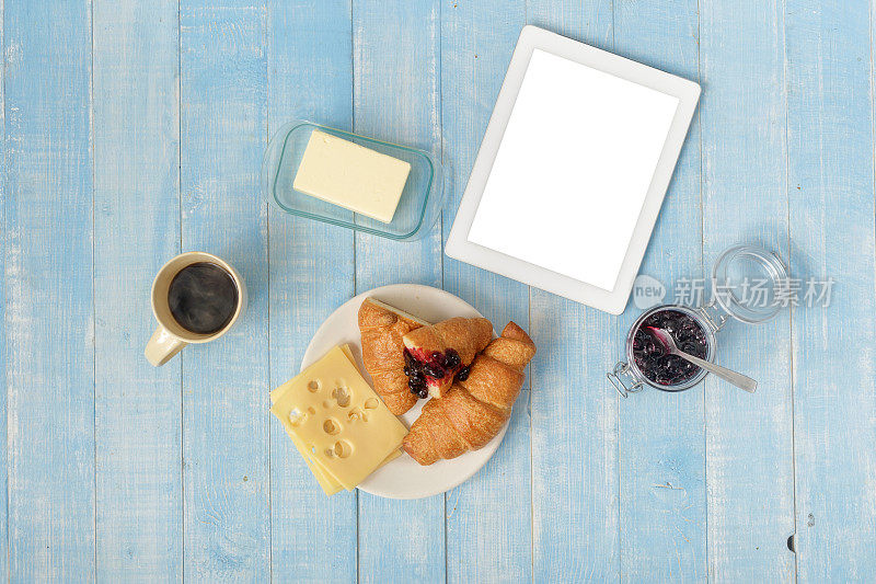 白色平板在家庭厨房与牛角面包，果酱，奶酪，黄油和咖啡，俯视图。早餐桌上的概念