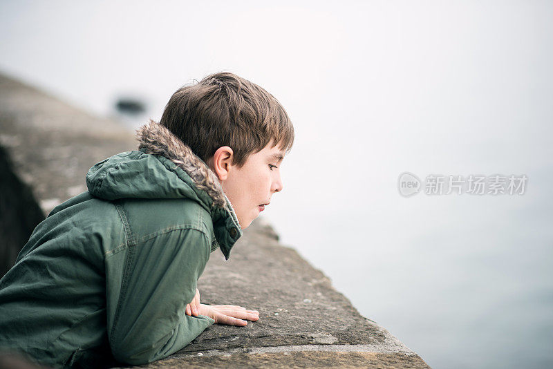 可爱的男孩看着栅栏那边的大海